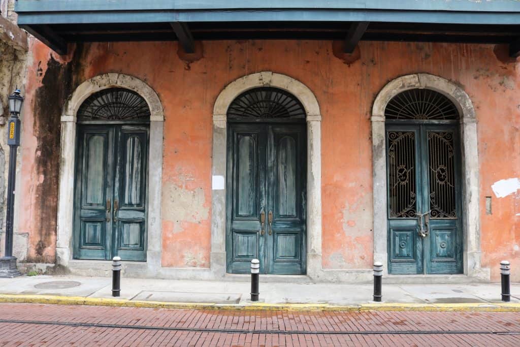An old and weathered building with three ornate doors. The doors are blue against a faded pink building. Located in Casco Viejo. 