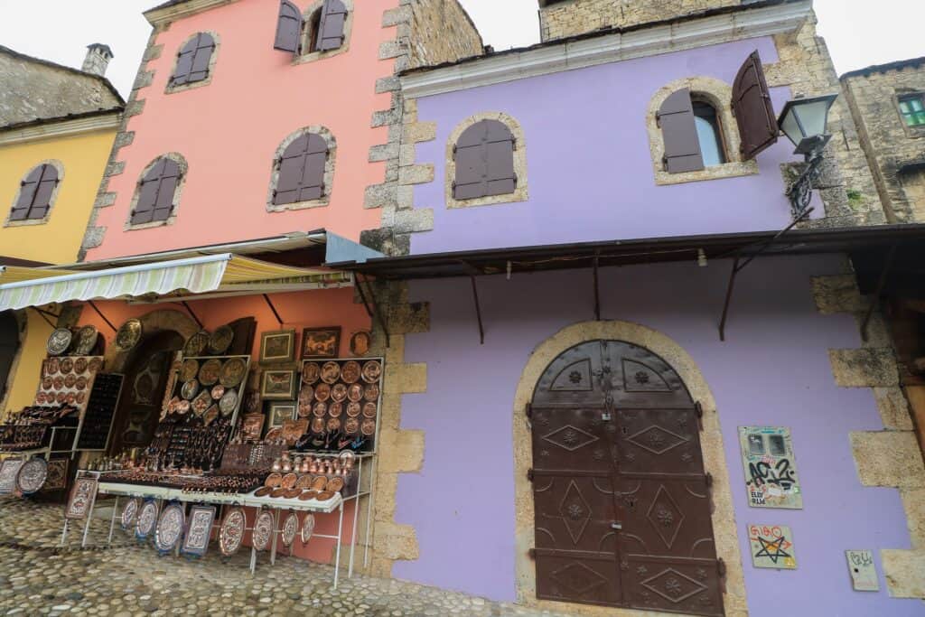 Mostar Old Town Bazaar, Čaršija with a pink and purple buildings and vendors selling wares.