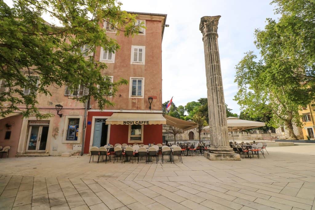 Adorable square near St. Simeon's Church in Zadar old town in Croatia with a cafe and tall stone pillar.