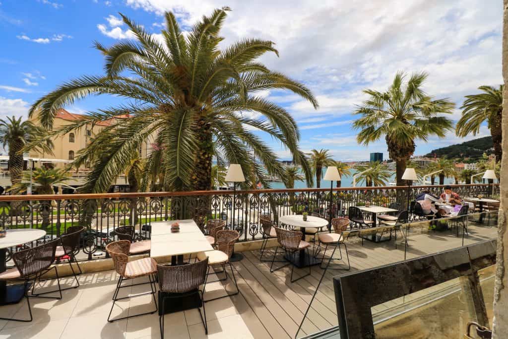 Dining along the Riva promenade at a restaurant patio, palm trees and view of the sea along Split's coast.