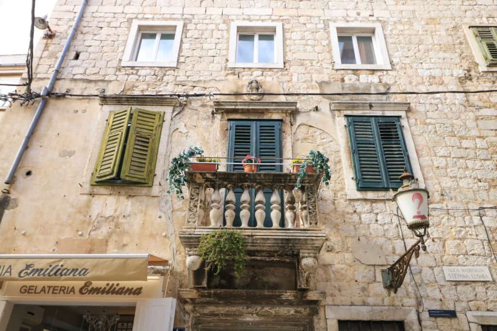 Looking up at a lovely small balcony with blue shutters of an old stone building that is a picturesque sight in Split, Croatia. 