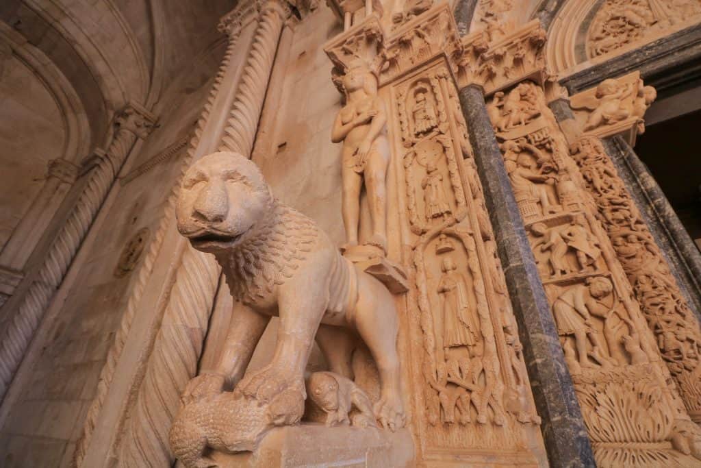 Detailed carving of a statue resembling a lion at the front entrance to St. Lawrence Cathedral with elaborate carvings in stone around the doorway in Trogir.