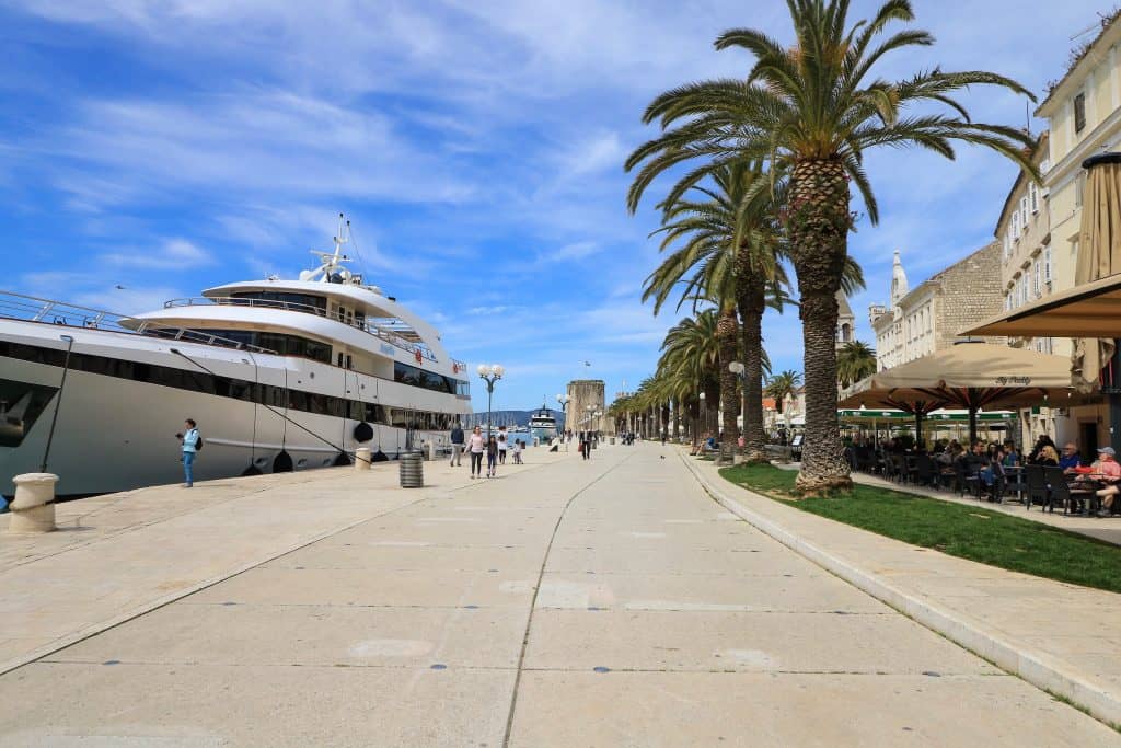 The beautiful riva or seaside Promenade lined with palm trees and restaurants on one side and yachts docked on the other side in Trogir old town in Croatia.