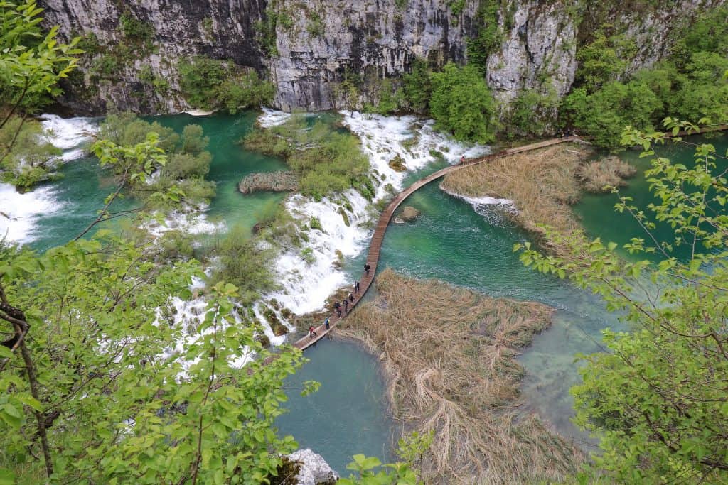 High up above near the entrance looking down at the view of Lower Falls from above with waterfalls and water on each side of a meandering boardwalk with people on it at Plitvice Lakes in Croatia.
