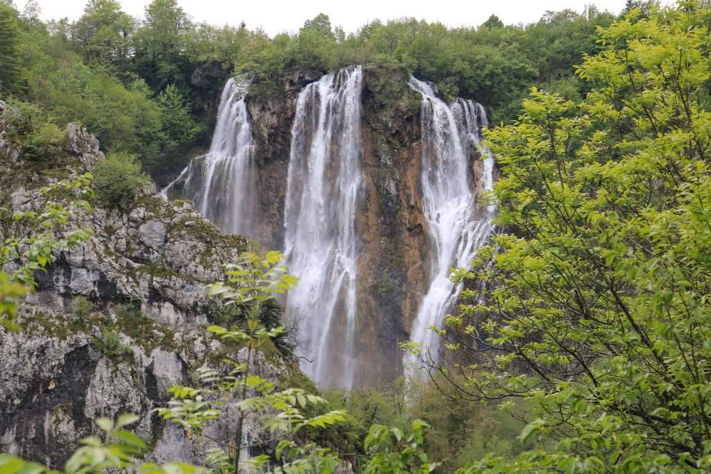 Standing at the base of the Great Waterfall or Veliki Slap which is very tall and impressive to see surrounded by dense green foliage at the Lower Lakes in Plitvice park.
