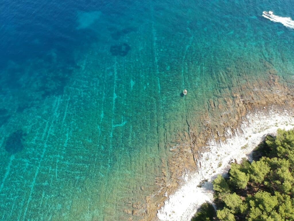 A drone view photo of a white sand beach with clear water in shades of blue in Trogir, Croatia.