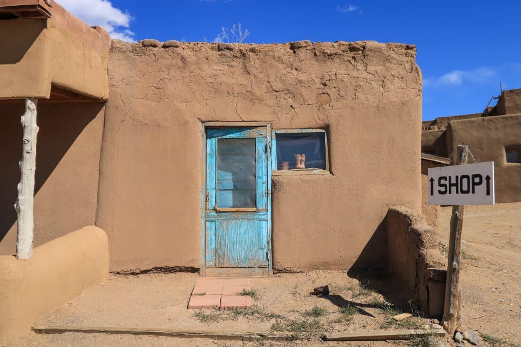 A small adobe house in tan color with a pale turquoise door at Taos Pueblo, one of the best day trips from Santa Fe,
