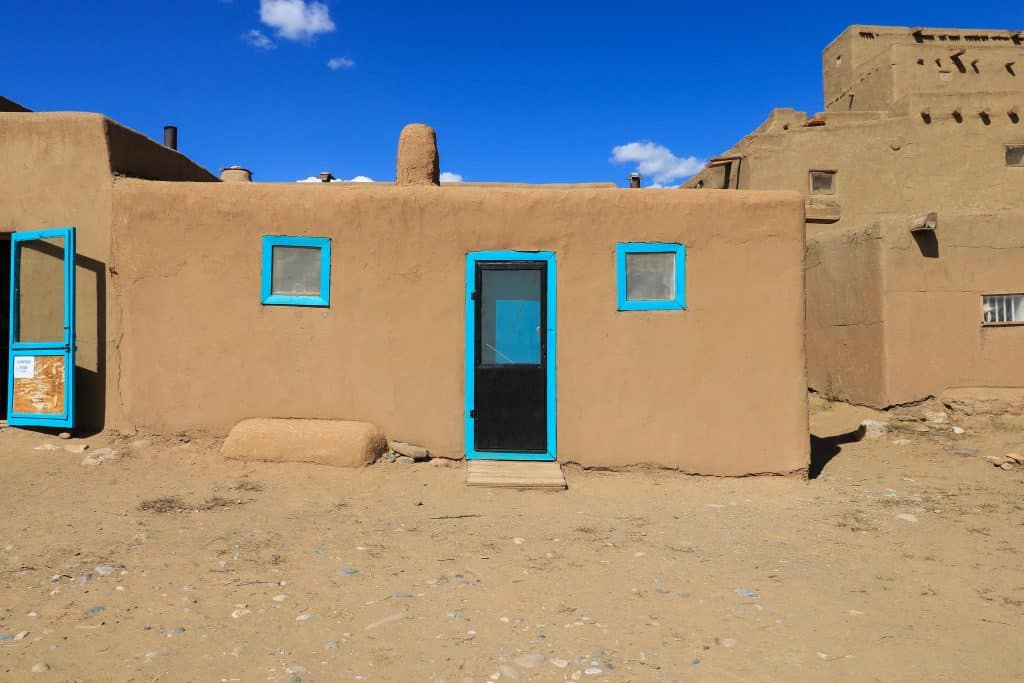 The only color you will see are pops of color on the doors or window trims against the tan adobe house on a sunny day in Taos Pueblo, New Mexico.