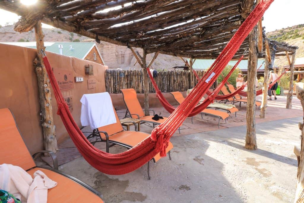 A row of orange hammocks underneath a natural wood overhang where people can relax after soaking in the mineral pools at Ojo Caliente Mineral Springs Spa.