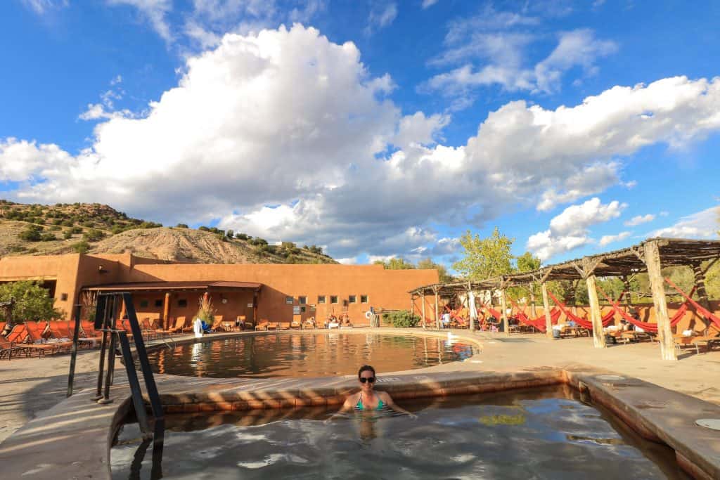 Sitting in the healing waters of the arsenic pool at Ojo Caliente Mineral Springs Spa with another pool behind me, several deck chairs, and canopies to sit under on a sunny day in New Mexico.