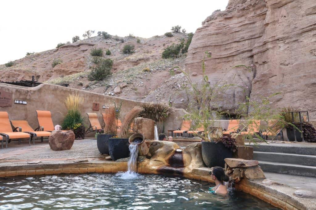 Jets of hot water are soothing to the back and shoulders pouring out of pots into a small mineral pool with lounge chairs and natural rock wall behind at Ojo Caliente Mineral Springs Spa.