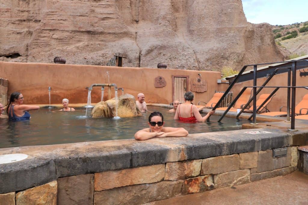 Sitting in one of the mineral pools enjoying the relaxing and soothing warm water with other guests in the background at the outdoor area of Ojo Caliente Mineral Springs Spa in New Mexico.