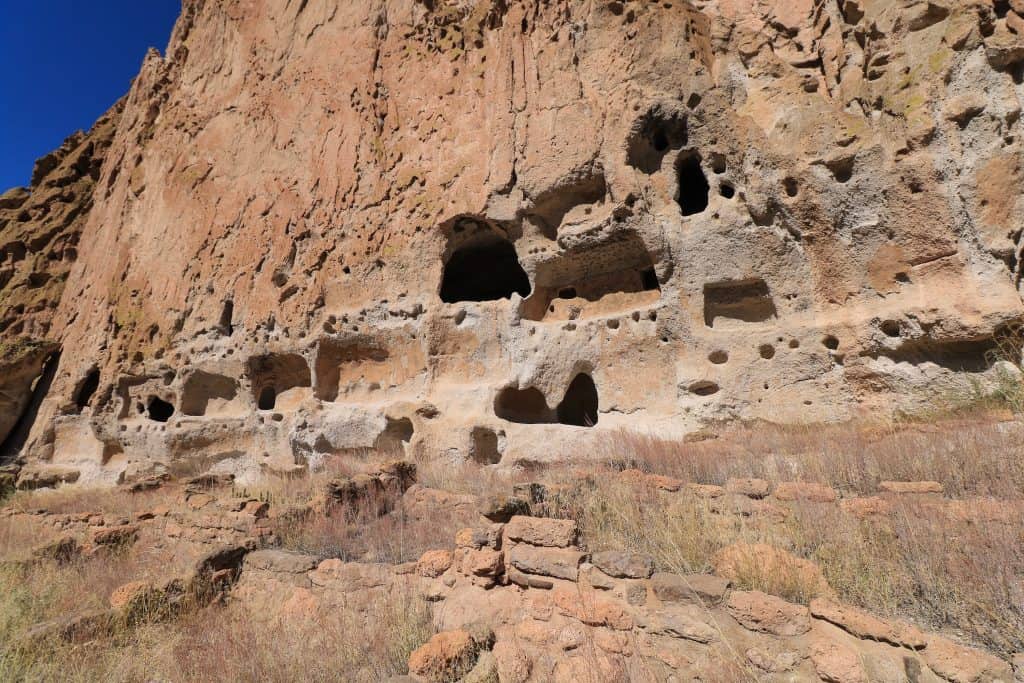 A close up of carvings into a wall of rock and dwellings of people from the past at Bandelier National Monument.