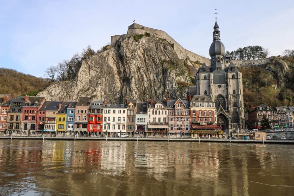 Citadel de Dinant sitting high up above the cathedral, colorful buildings in town below, and the Meuse River in Dinant, Belgium.