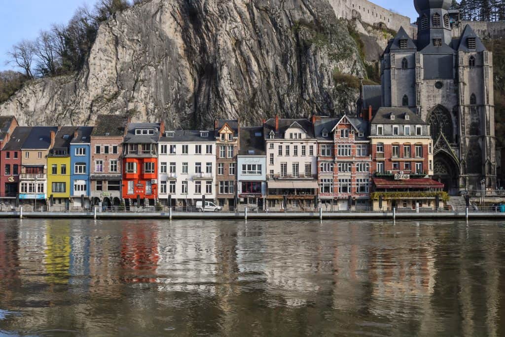 A zoomed in view of the colorful buildings in red, blue, white, and yellow across the Meuse River at the base of the sheer cliffs where the citadel sits in Dinant, Belgium.