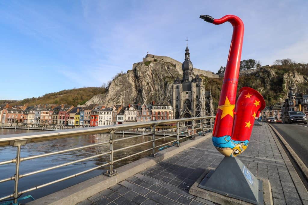 A red saxophone statue on the Charles de Gaulle bridge, one of several colorful saxophones lining the bridge and waterfront in Dinant, Belgium.