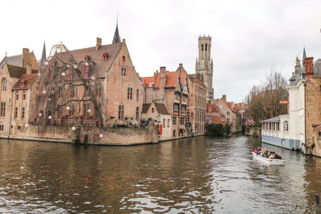 A boat ride setting doesn't get more idyllic than this with a small boat of people on the canal surrounded by beautiful buildings in Bruges.
