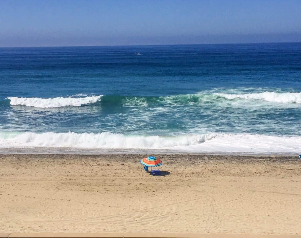 Looking down at a beautiful stretch of golden sand, a beach chair with colorful umbrella, and the Pacific Ocean at one of the most popular beaches in San Diego, California.