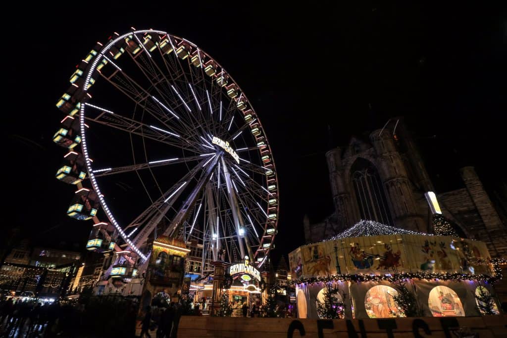 A huge Ferris wheel and market stalls lit up at night