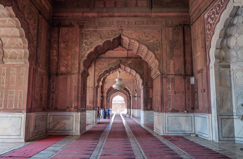 A long open-air corridor in Jama Masjid in Old Delhi, India with an arched walkway and carpets throughout