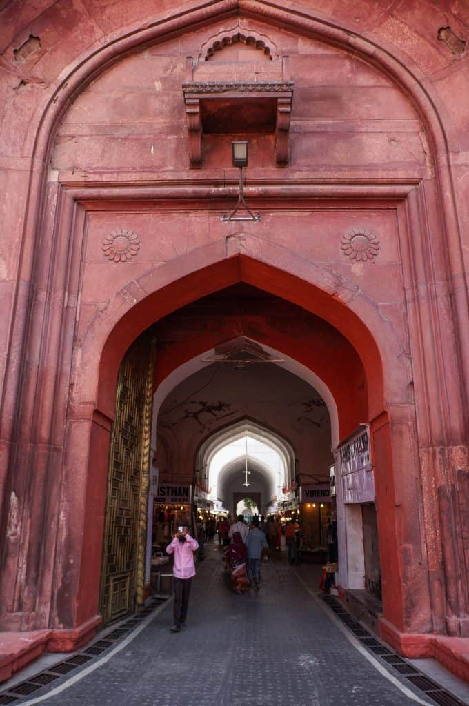 The very tall Lahore Gate entrance of the Red Fort in Delhi made of a deep red sandstone and shops lining the corridor into the complex