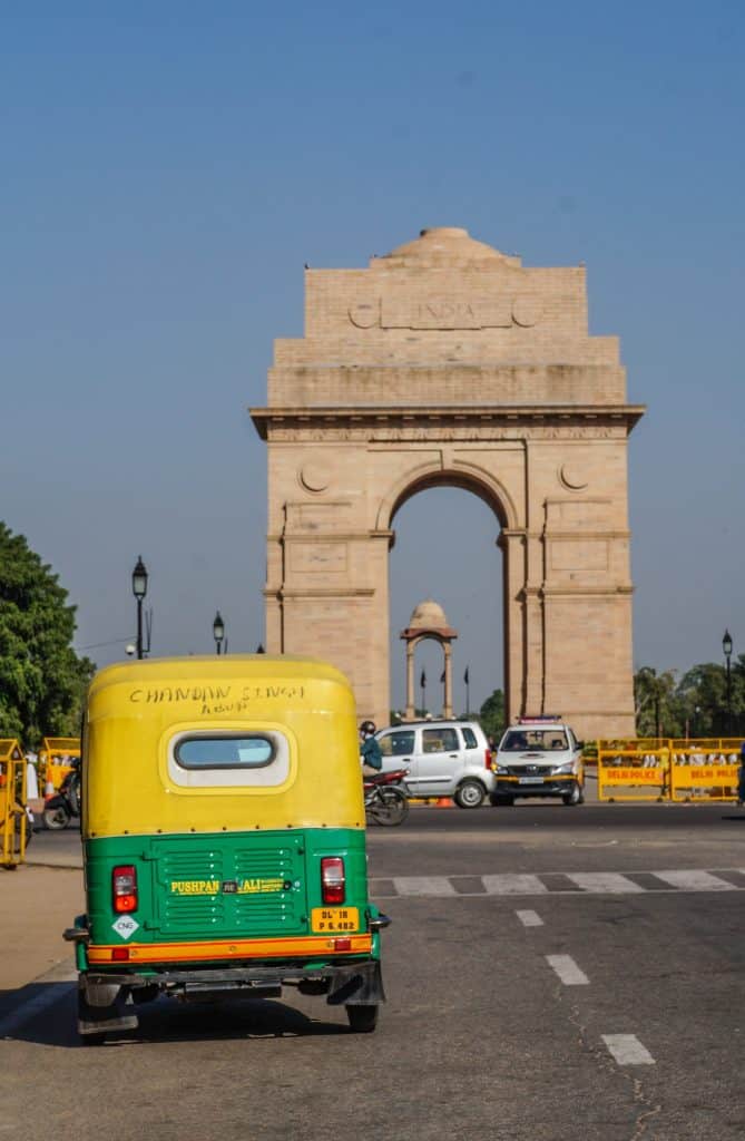 A bright green and yellow autorickshaw in front of the tan colored India Gate arched memorial