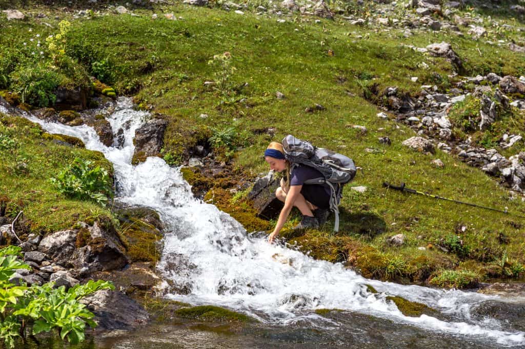 A girl leaning down to fill up her filtered water bottle in a running stream