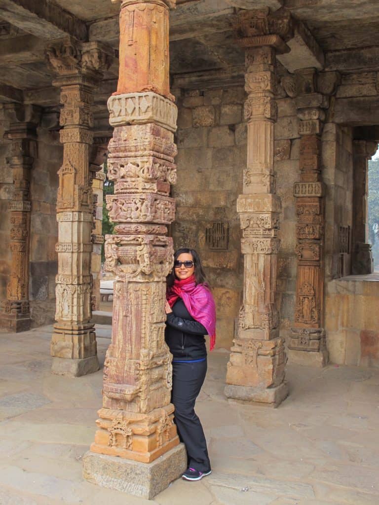 Me standing next to an intricately carved pole within the temple at Qutub Minar in Delhi is one of the most popular Delhi attractions to see