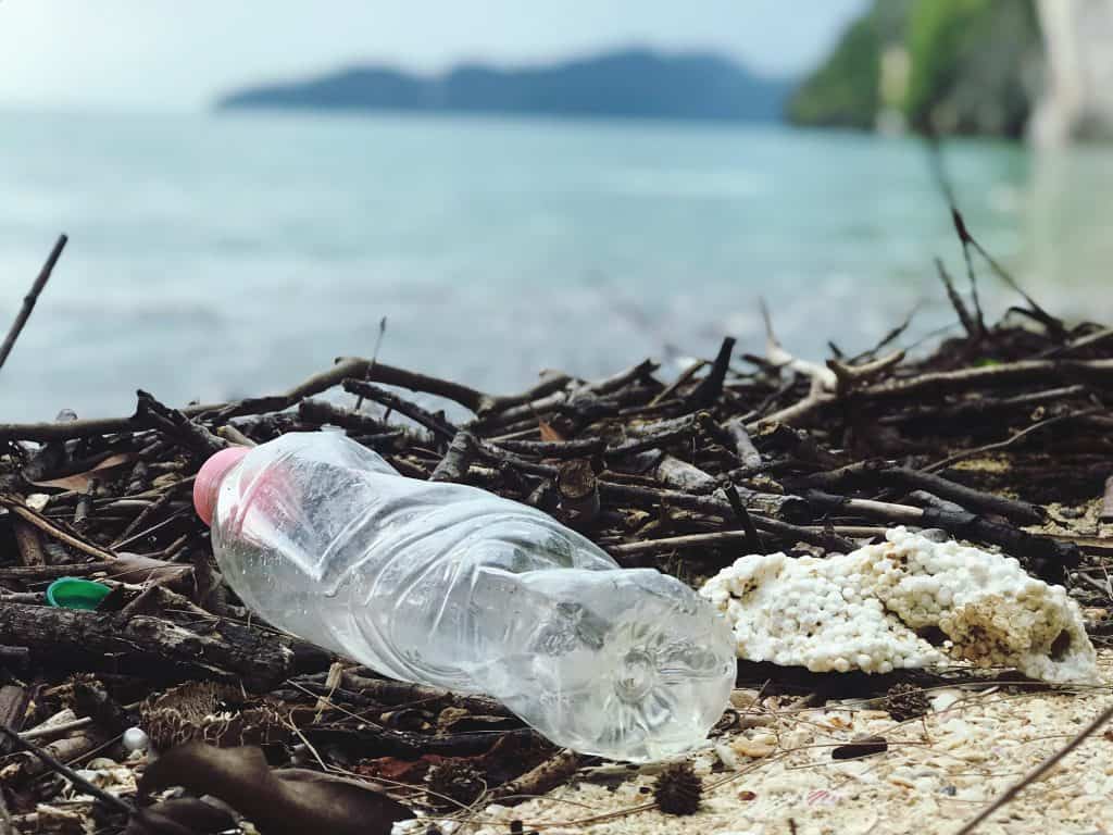 a used one-use plastic water bottle thrown as trash onto a beach