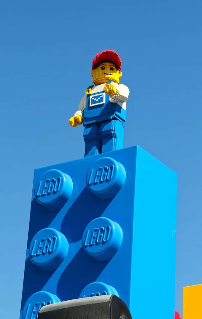 A brightly colored Lego man standing on top of a blue Lego building block