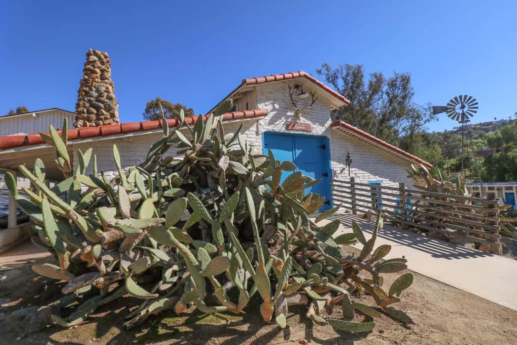 The old stable and bunkhouse that is all white and with a bright turquoise door surrounded by cacti