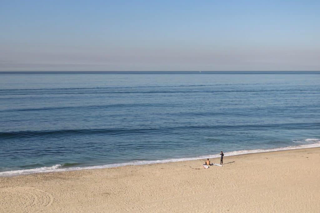 Two surfers sitting on Carlsbad Beach waiting for the waves to come before heading out