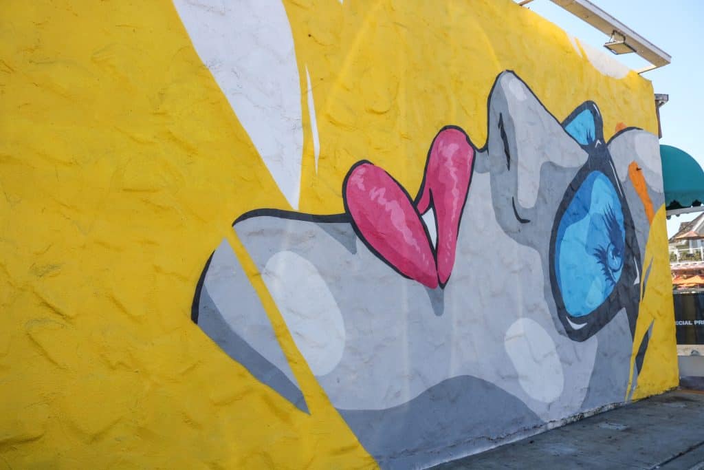 A bright yellow art mural with a side profile of a girl wearing sunglasses and hot pink lipstick
