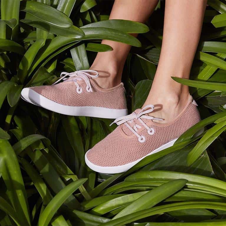 A pair of Allbirds shoes in a pale pink with white sole among green plant foliage. Photo used with permission by Allbirds