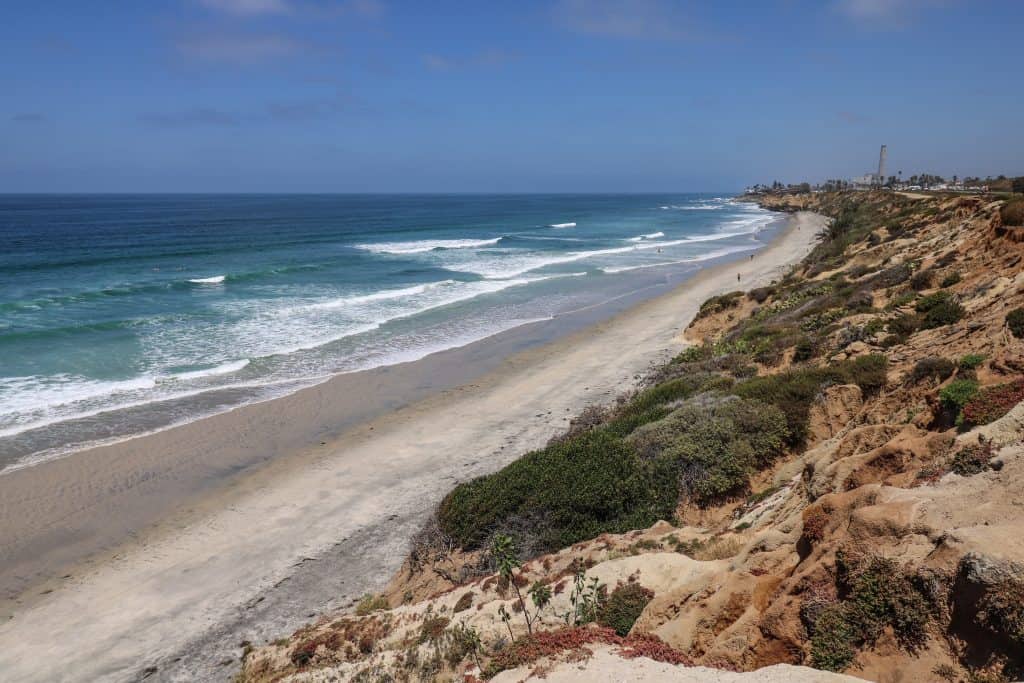 Looking south to north up the coastline in Carlsbad on a sunny day with turquoise blue water and sandy b