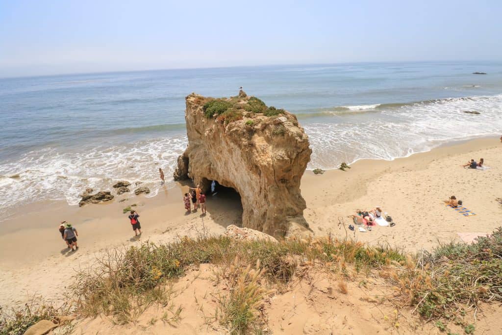 Looking down at the largest rock formation at El Matador Beach with people taking photos and enjoying the sunny beach day.