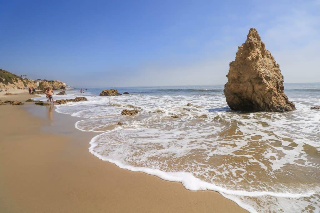 A large rock with a pointed tip like an arrow sits right along the shoreline with the water brushing the golden sand at El Matador State Beach which is one of the best beaches in Malibu.