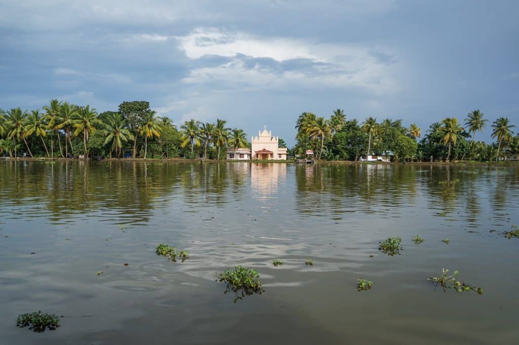 A peachy pink church sitting on the banks of the backwaters of Kerala surrounded by lush palm trees.
