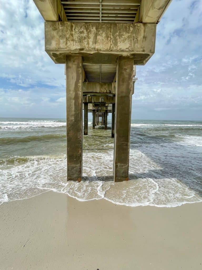 Looking straight through the pillars of the Orange Beach Pier with the waters of the Gulf Coast splashing.
