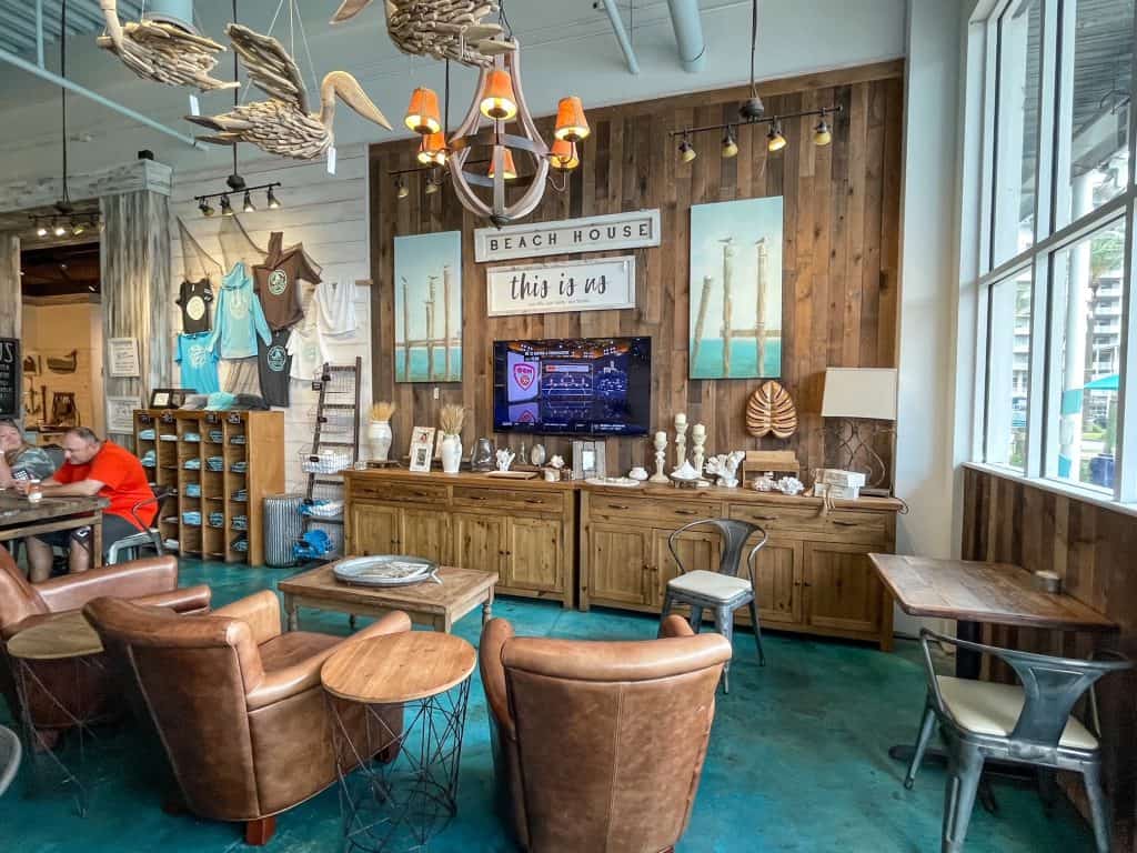 The charming living room feel inside The Southern Grind with tan leather chairs, coffee table and TV.