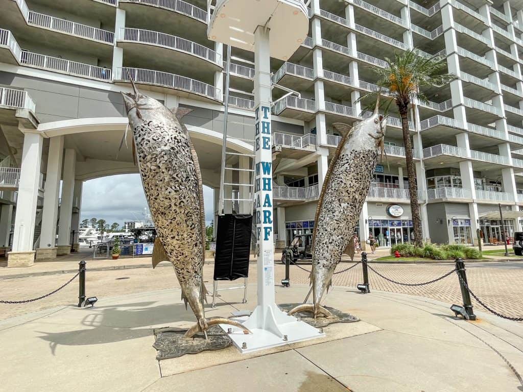 Two metal swordfish statues with The Wharf sign between the marina and shops.