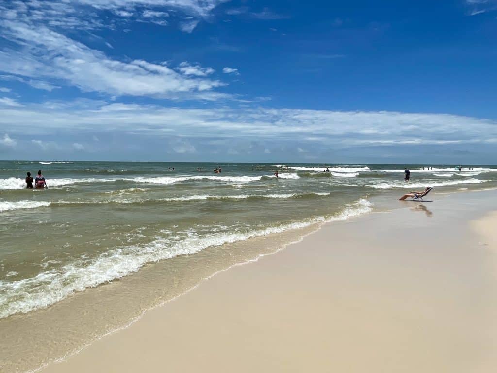 A woman sunbathing in a beach chair that is on the shoreline where the ocean water meets the sand on a sunny day.