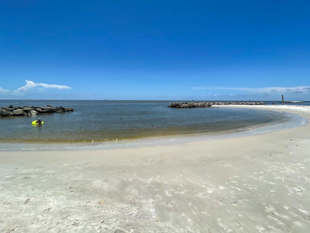 The white sand beach along Pelican Point Beach that forms a crescent shape with a shallow swimming area.
