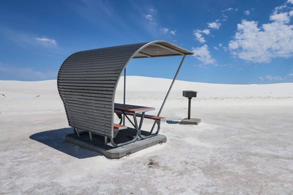 A cool metal space age picnic table with overhead covering surrounded by white sand.