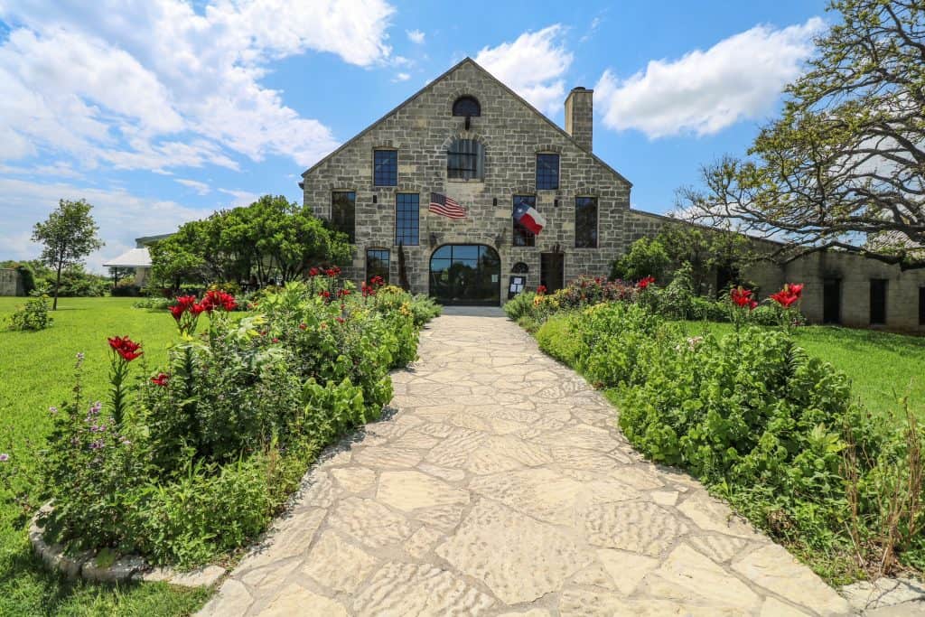 View of the front entrance of Becker Vineyards that is made of stone and a lined walkway of flowers.