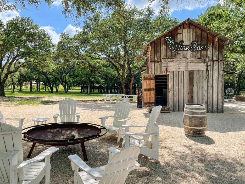 A small wooden barn that serves as a wine bar and outdoor white wooden seats surrounding a fire pit.