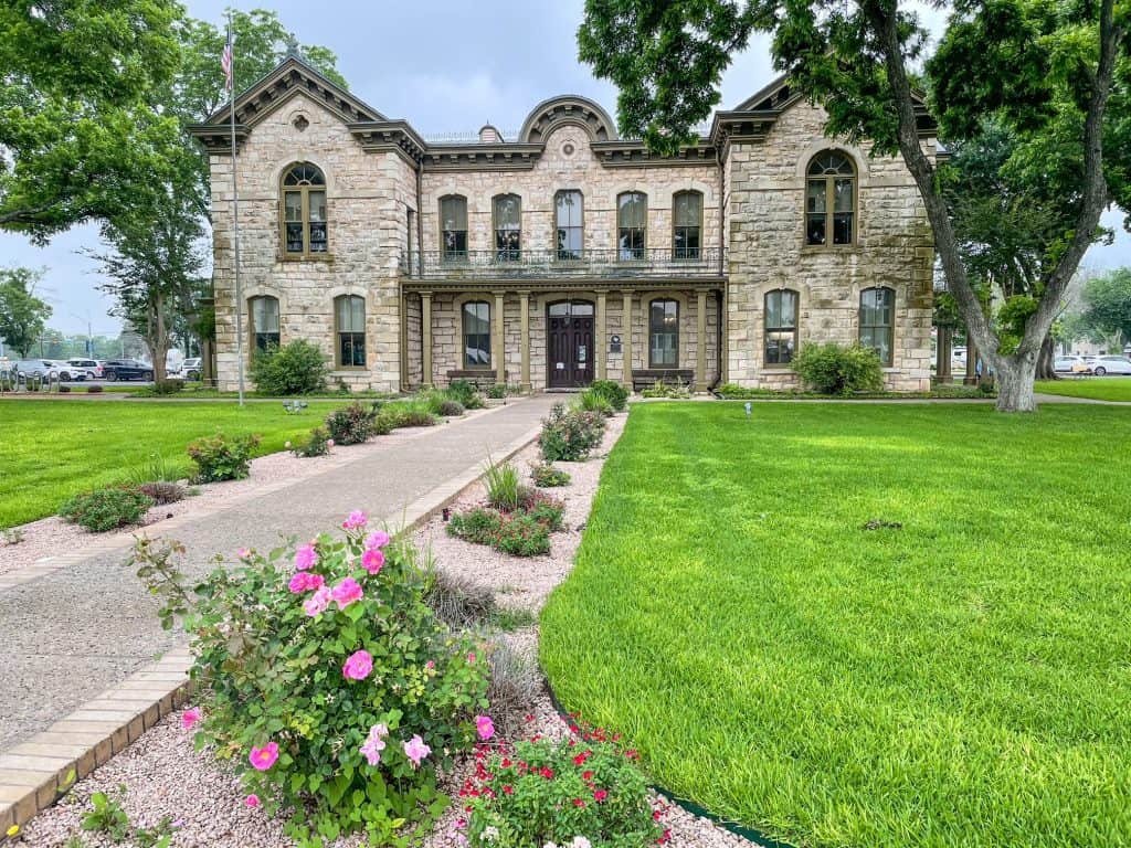Pink flowered walkway leading to the old stone German-styled building that is now the library in Fredericksburg.