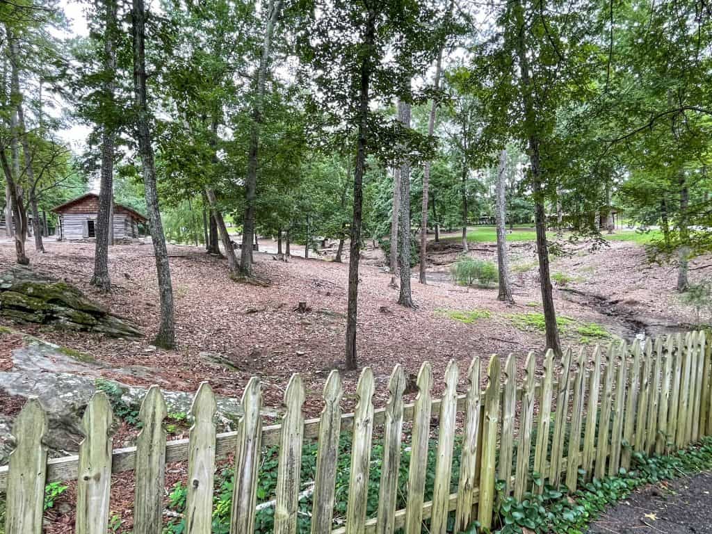 View of the forest and cabins bordered by a picket fence while riding the mini train in Noccalula Falls Park.