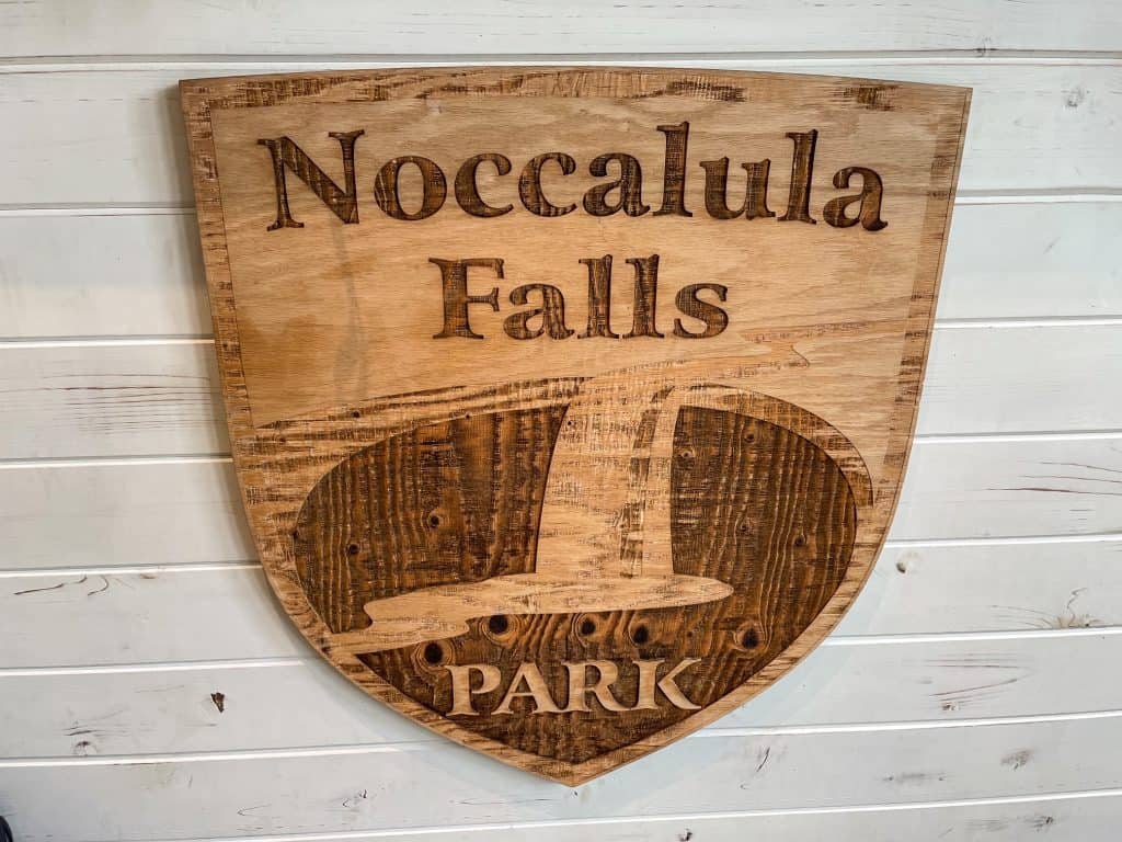 A sign made of wood with the words Noccalula Falls Park and an image of Noccalula Falls.