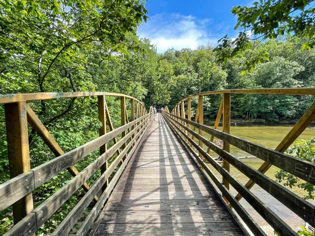 Walking across a wooden bridge that runs over the river at High Falls in Alabama and surround by lush forest on each side.